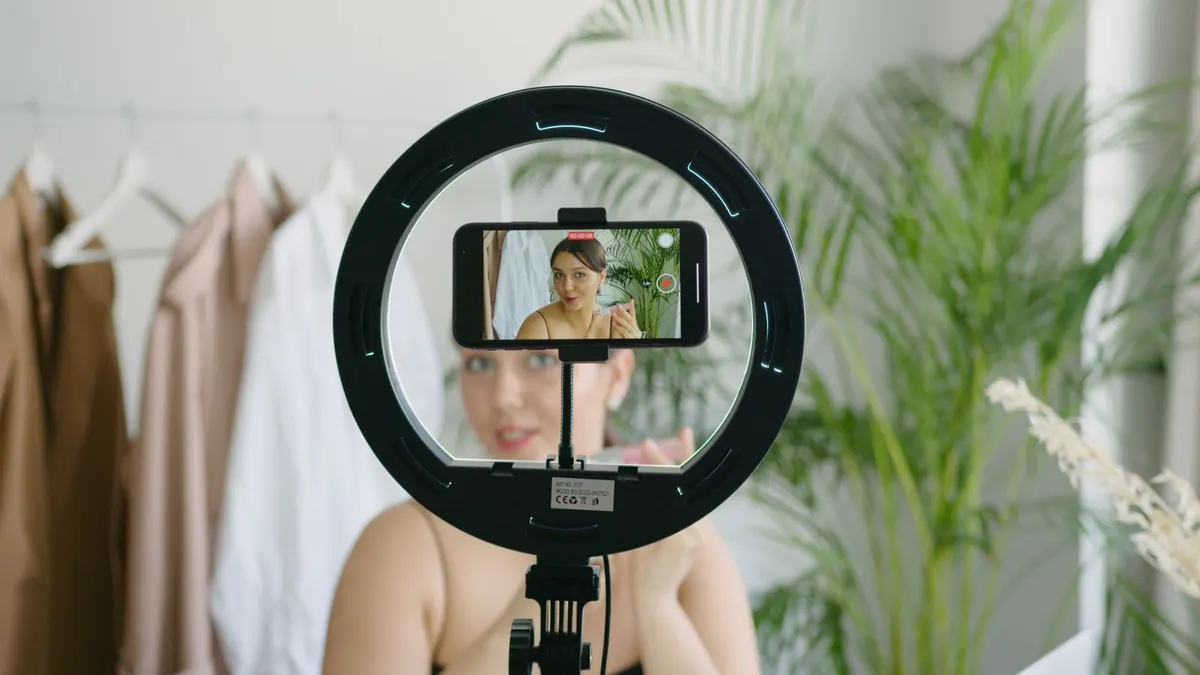 A phone mounted inside a ring light, filming a woman who is sitting in front of a clothes rail.