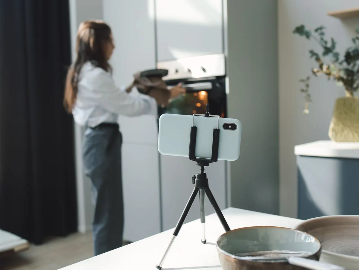 A smartphone mounted on a tripod, filming someone working at a kitchen counter.