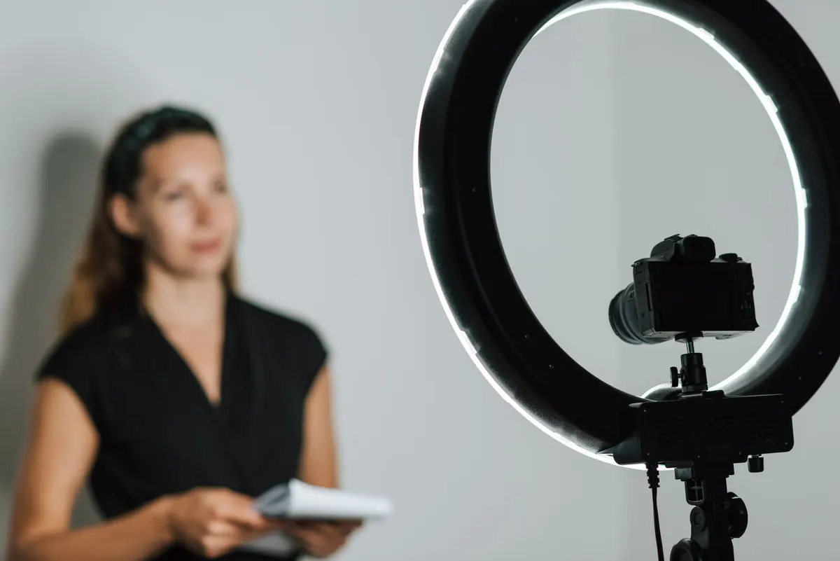 Someone speaking to a camera on a tripod while holding a notepad, against a plain backdrop.