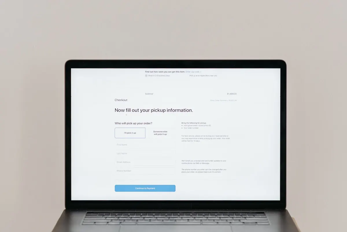 A laptop showing a checkout page with a pickup information form and a continue to payment button.