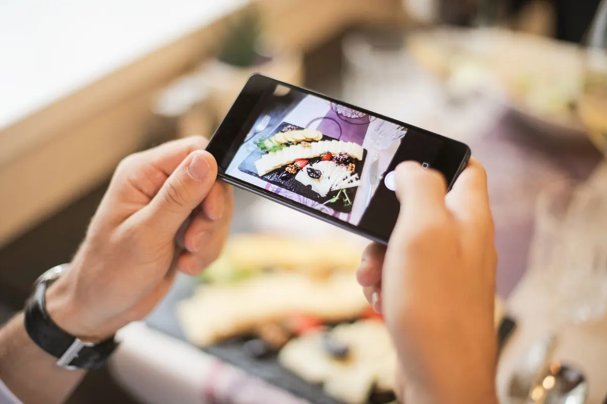 Two hands holding a phone horizontally, framing a plate of food on a table.