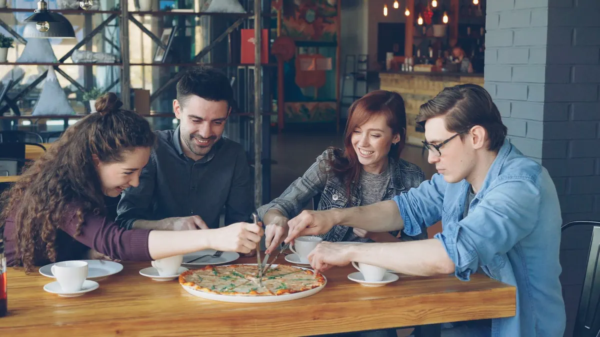 Four young adults sharing a pizza around a cafe table.