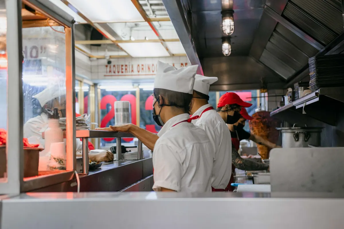 Cooks in white jackets and caps working along a busy service counter.