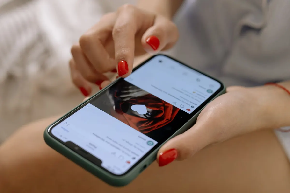 A close-up of a woman with red painted nails holding a smartphone and scrolling with her thumb.