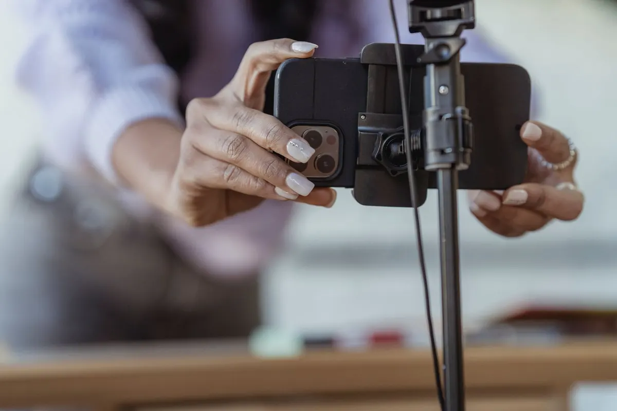 Two hands clamping a phone into a tripod mount, the phone held horizontally in the bracket.