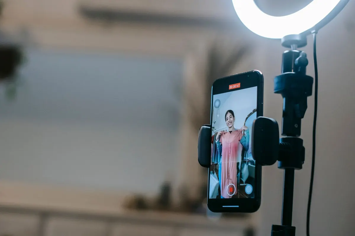 A phone clamped beside a lit ring light, its screen showing a woman holding up a dress while recording.