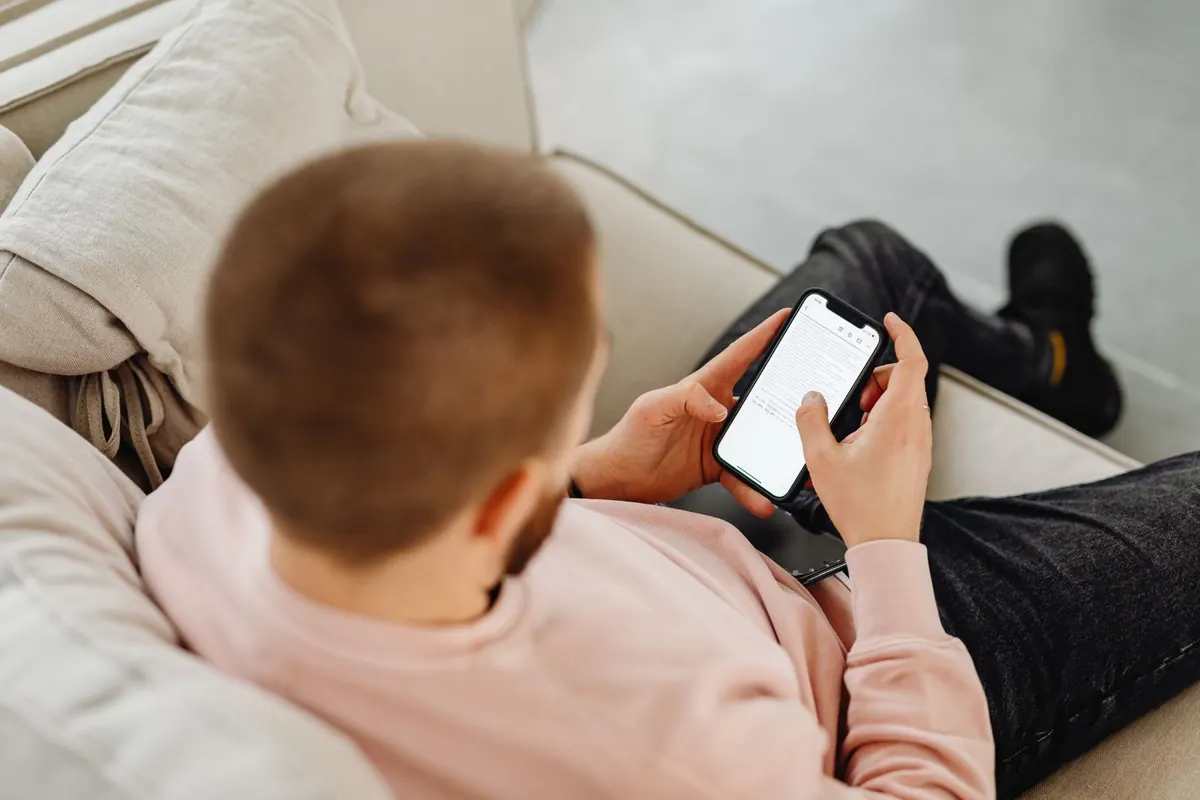 Seen from behind and above, a man slouched on a sofa holding a phone.